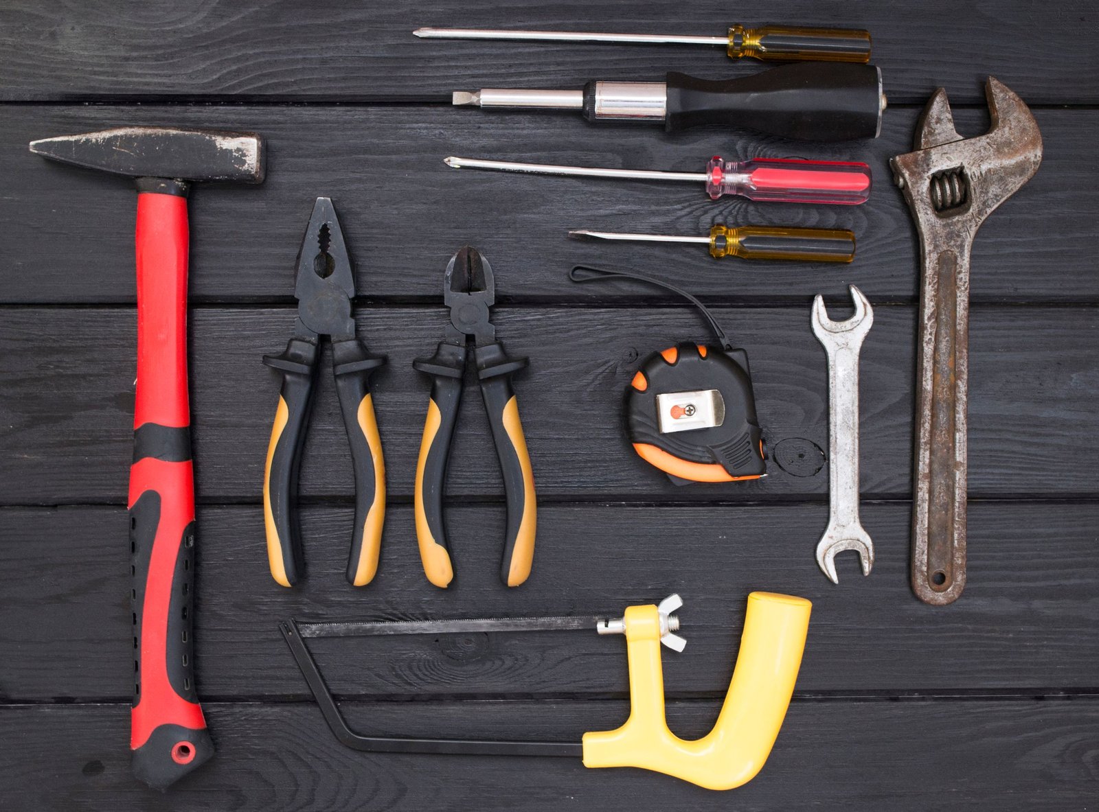 A flat lay photograph of various hand tools on a black wooden surface, ideal for workshops.