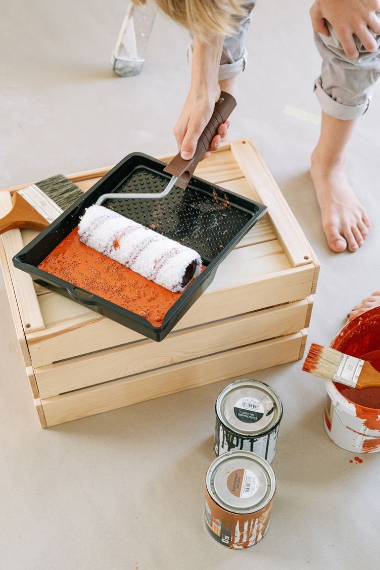Hands using a paint roller on a DIY project with paint cans and brushes.